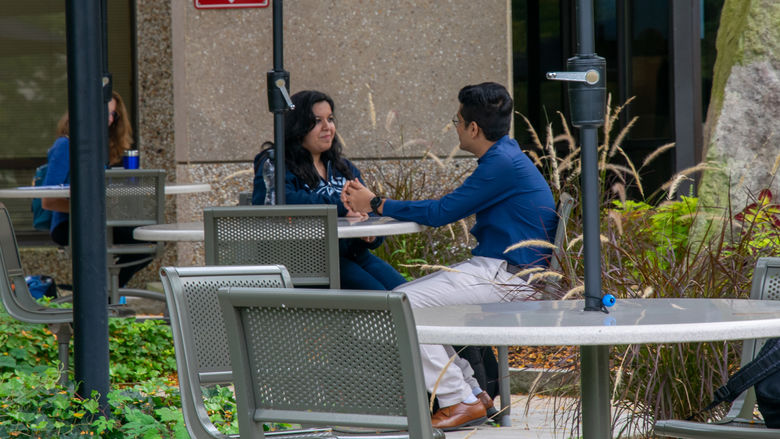 Two students sitting at an outdoor table talking