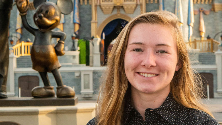 Hannah Schneidewind poses for a photo behind a Disney castle and a statue of Mickey Mouse to the left of her