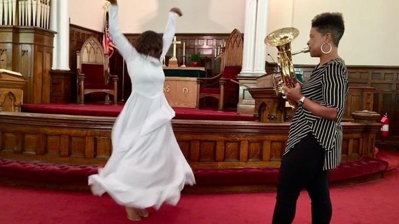 A woman dancing while another woman plays a tuba