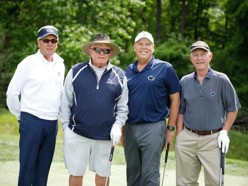 Four golfers stand on a course with their golf clubs. 
