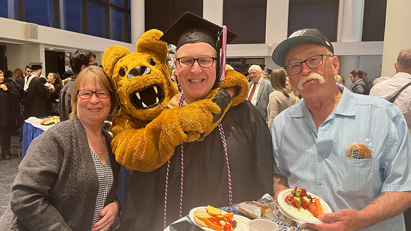 Jason Herman being hugged by the Nittany Lion with his parents next to him