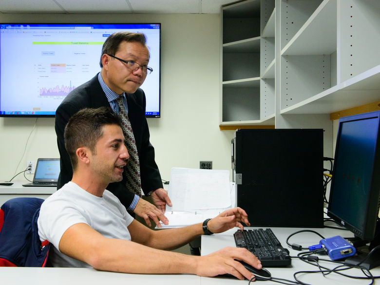 A student shows a professor his work on a computer