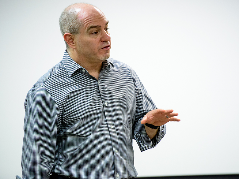 A male professor speaks in front of a blank white board