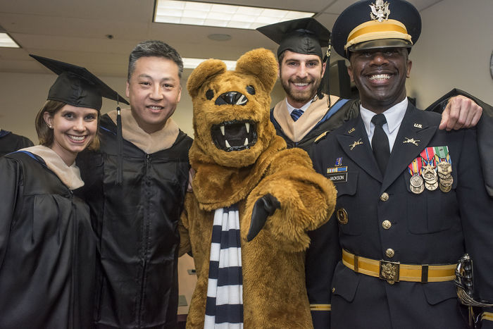 Four students wearing graduation robes standing with the Nittany Lion