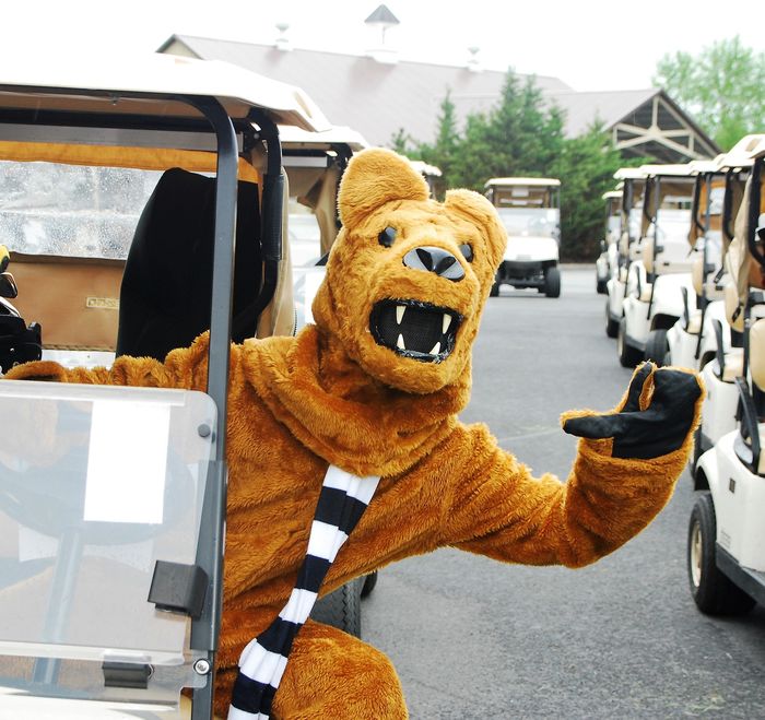 The Nittany Lion leans out of a golf cart and waves.