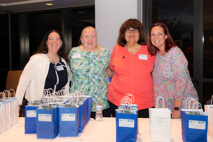 Four women stand behind a table with gift bags at Great Valley's commencement ceremony.