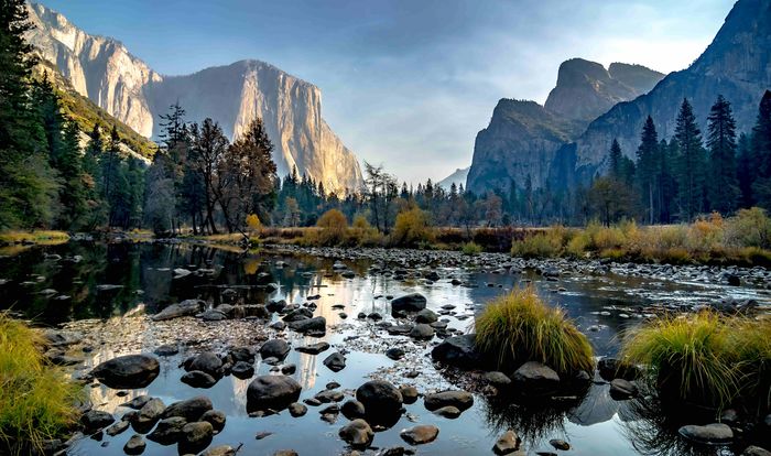 Early morning at Yosemite National Park, with sunlight on mountains and rocks and grass poking out of a lake