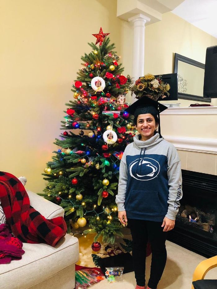 Anshul Sarvate, wearing a Penn State sweatshirt and a graduation cap, stands in front of a Christmas tree