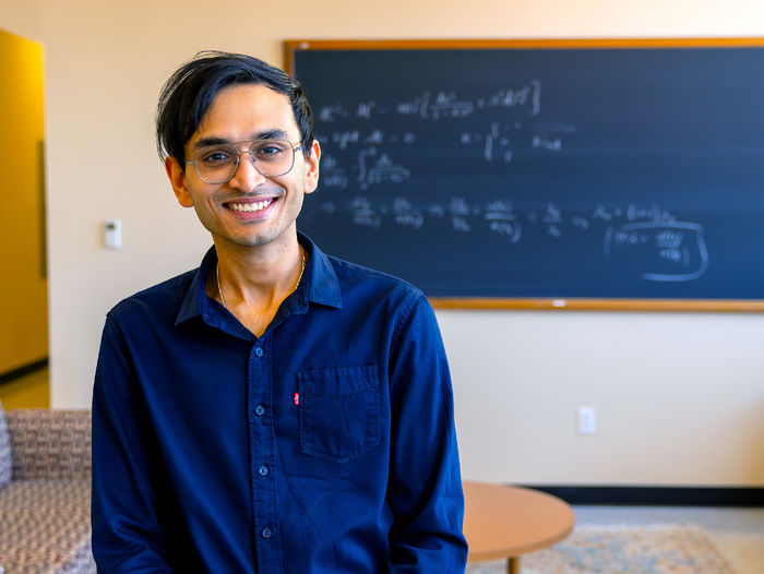 person smiling at camera with out of focus chalkboard in background