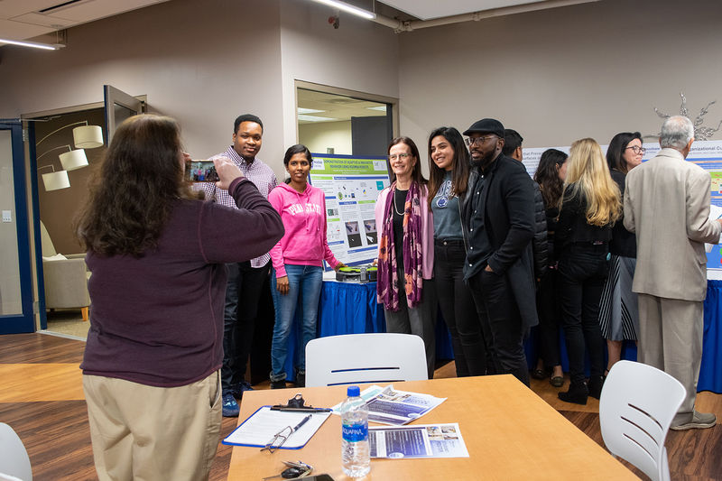 Students and their faculty adviser pose with their poster in the background as a a photo is taken in the foreground