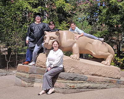 Two adults and two children pose in front of the Nittany Lion Shrine.