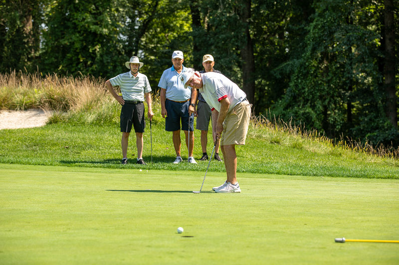 A man hits a golf ball while 3 other men watch