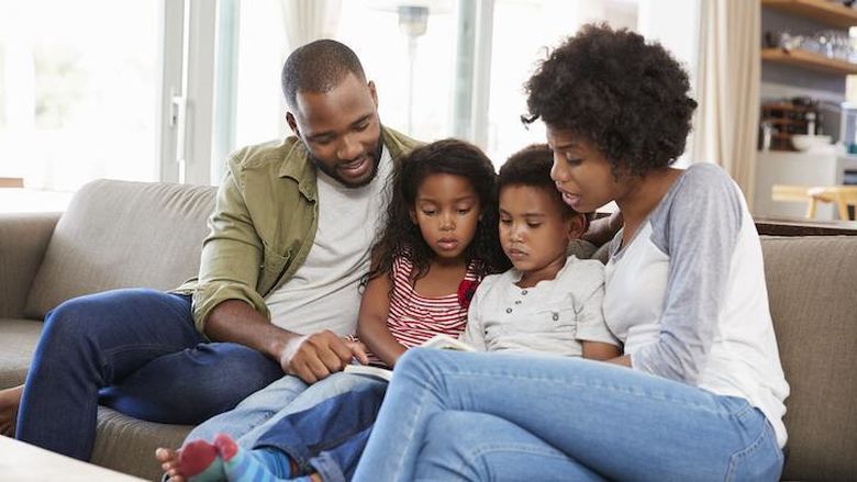 Young black family sitting on the couch reading a book.