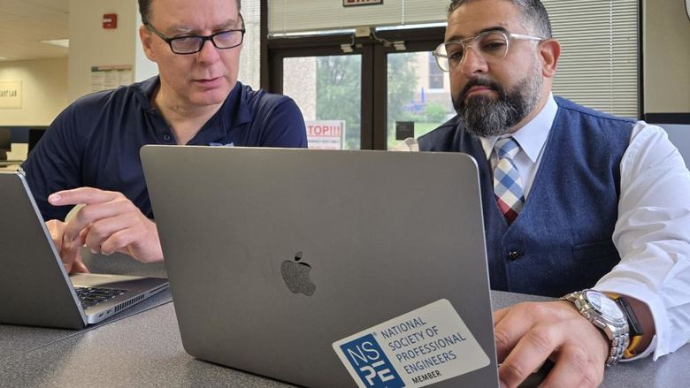 Two people collaborate on a project while working on laptops in a computer lab