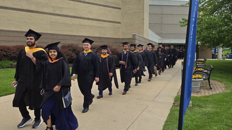 Master's degree graduates walk outside in a line to the commencement ceremony