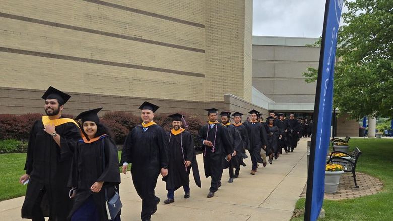 Master's degree graduates walk outside in a line to the commencement ceremony