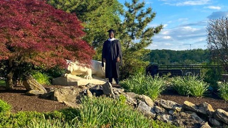 Jonathan Adrien standing by the Nittany Lion statue