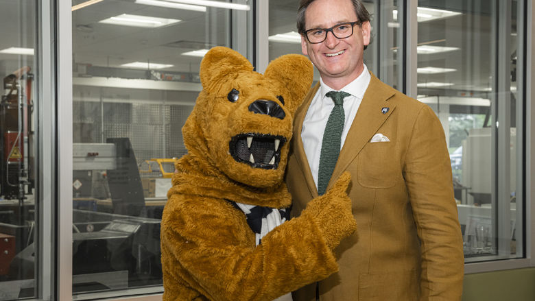 Colin J. Neill smiles and poses with the Nittany Lion