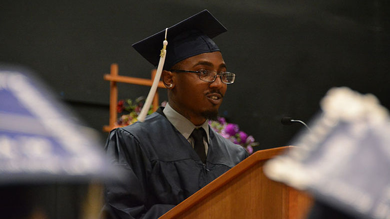 Alijah Hasan-Douglas speaks at a podium in his graduation cap and gown. 
