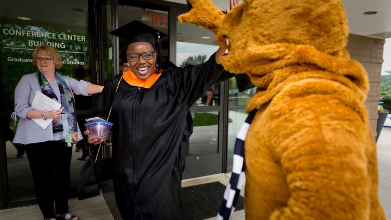 A graduate student shares a high five with the Nittany Lion prior to spring commencement at Penn State Great Valley