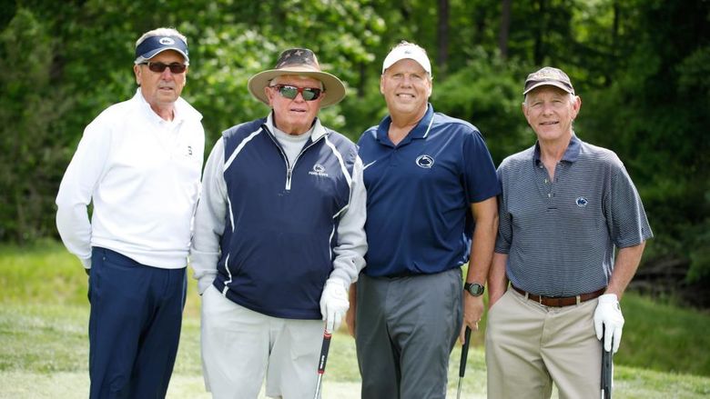 Four golfers stand on a course with their golf clubs. 
