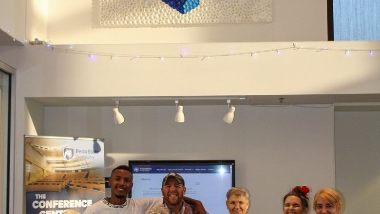 A group of people stand in front of a Nittany Lion mural made of bottle caps