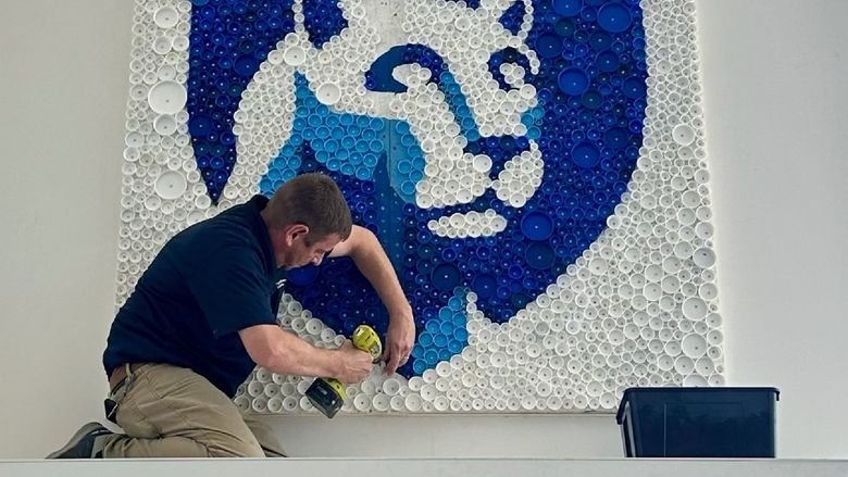 A person uses a drill to install a Nittany Lion mural