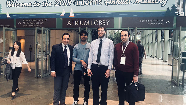 Mohamad Darayi, Devendra Jaiswal, Scott Clayman and Ashkan Negahban standing in front of the INFORMS conference sign