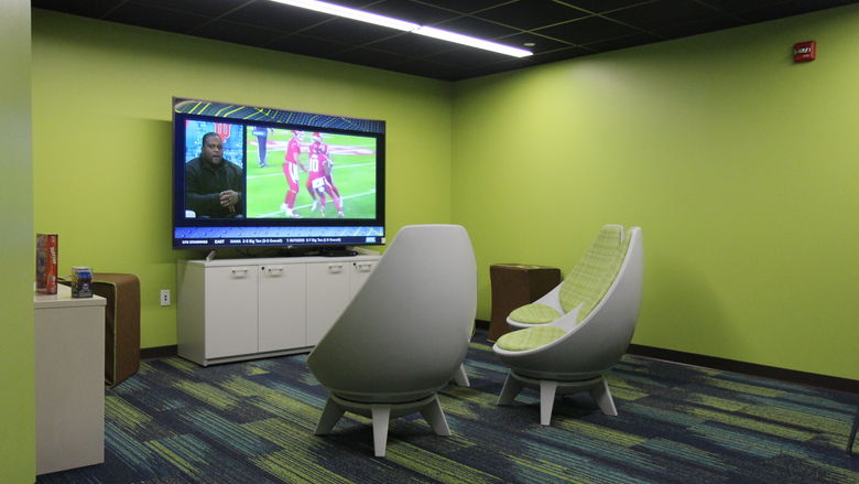 Three rounded chairs face a large television that shows a football player