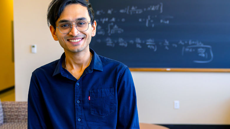 person smiling at camera with out of focus chalkboard in background