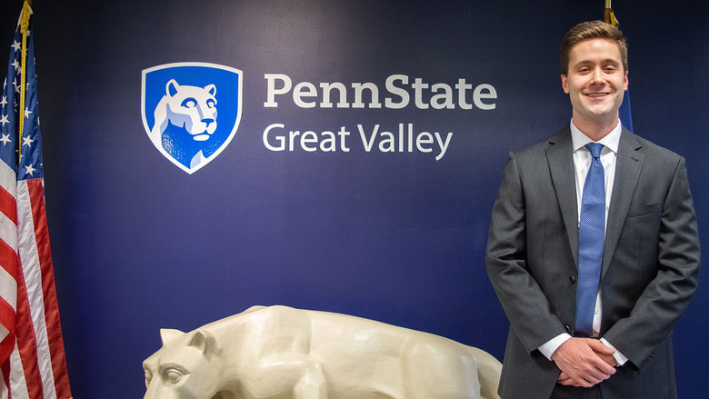 John Boland standing next to a Nittany Lion statue under the Penn State Great Valley logo