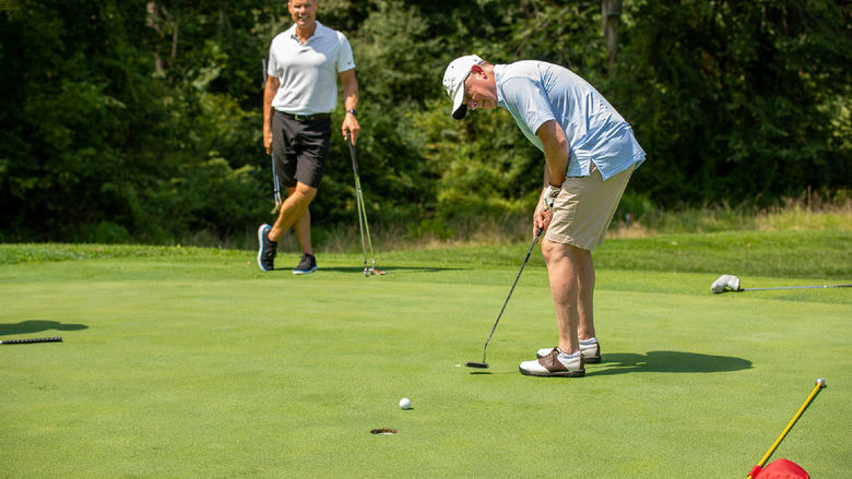 A man hits a golf ball while another man watches