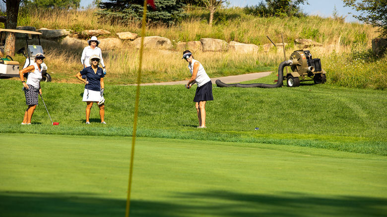 A woman hits a golf ball while 3 other women watch