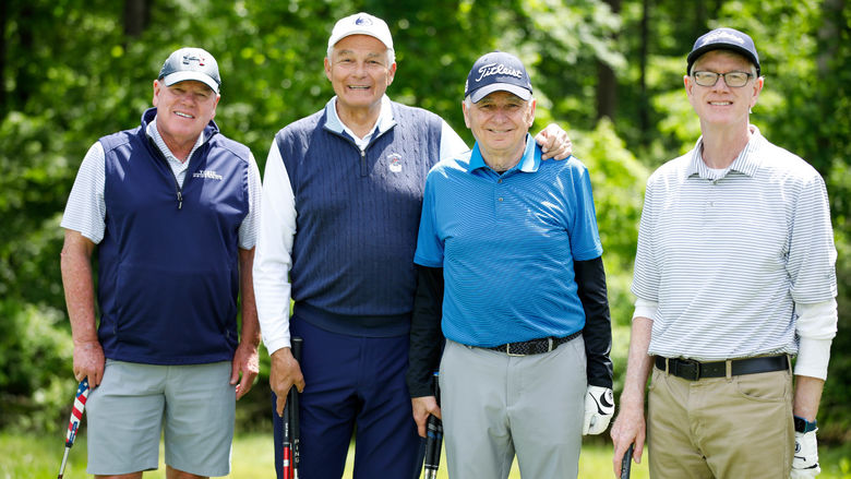 Four golfers stand together on the green with their clubs. 