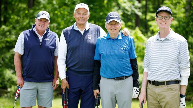 Four golfers stand together on the green with their clubs. 