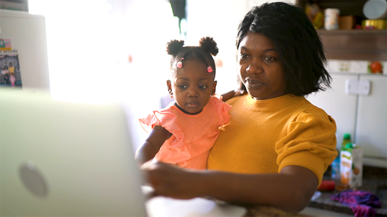 A woman holds a toddler as they sit in front of a laptop