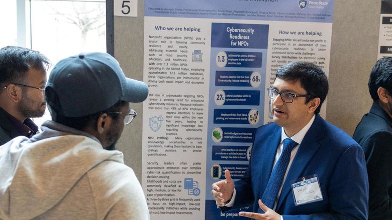 Two master's students explain their nonprofit cybersecurity research project to a visitor