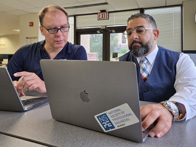 Two people collaborate on a project while working on laptops in a computer lab