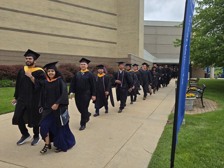 Master's degree graduates walk outside in a line to the commencement ceremony