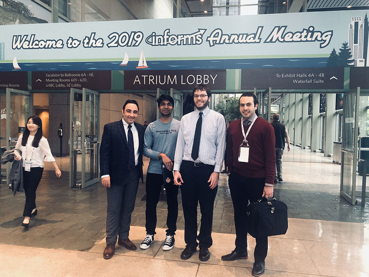 Mohamad Darayi, Devendra Jaiswal, Scott Clayman and Ashkan Negahban standing in front of the INFORMS conference sign