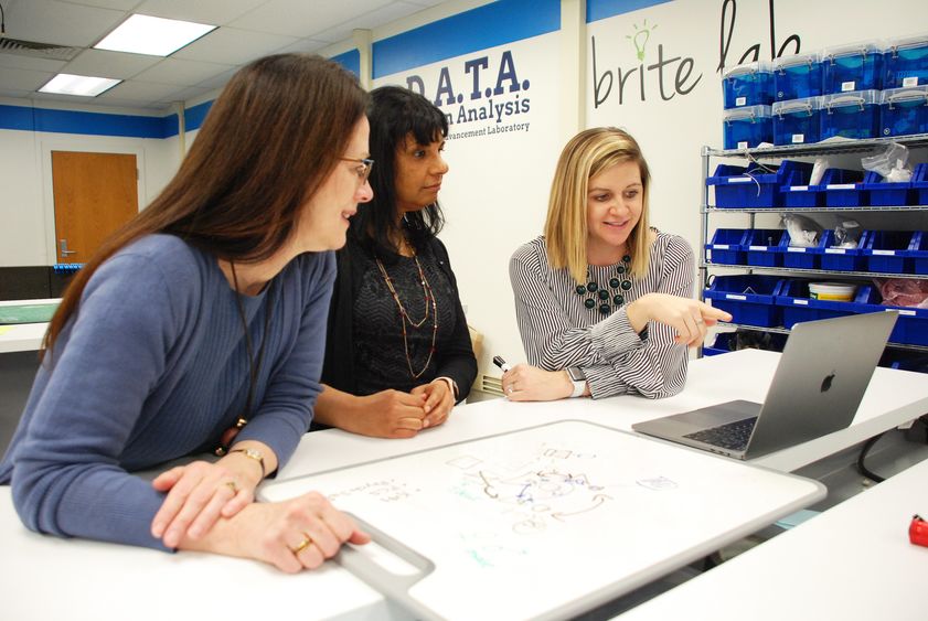 Two women looking at a computer screen as another woman points to the screen