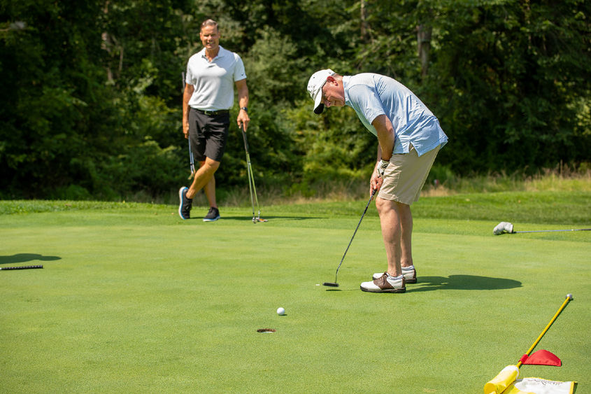 A man hits a golf ball while another man watches