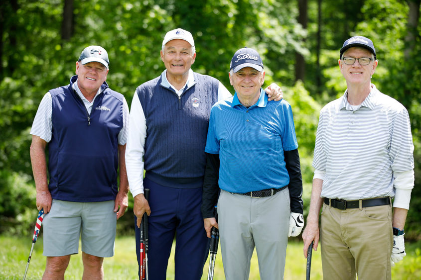 Four golfers stand together on the green with their clubs.