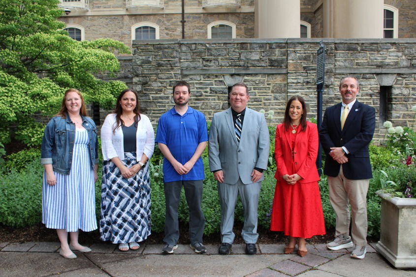 A group of six individuals pose in front of a stone wall